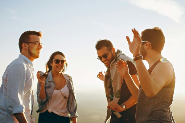 A group of four friends enjoy a sunny day, laughing and conversing outdoors with a bright sky in the background.