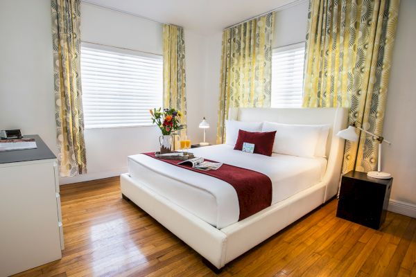 A modern bedroom with a white bed, red accents, floral curtains, and a tray with flowers and drinks on the bed.