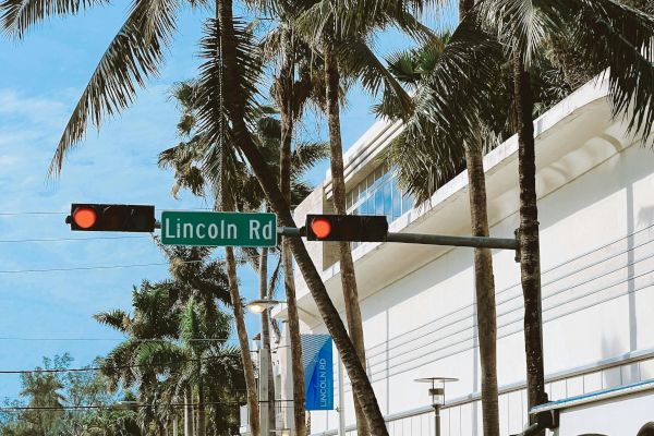 A street scene with palm trees, cars, and a sign for Lincoln Rd. Traffic lights and buildings are also visible.