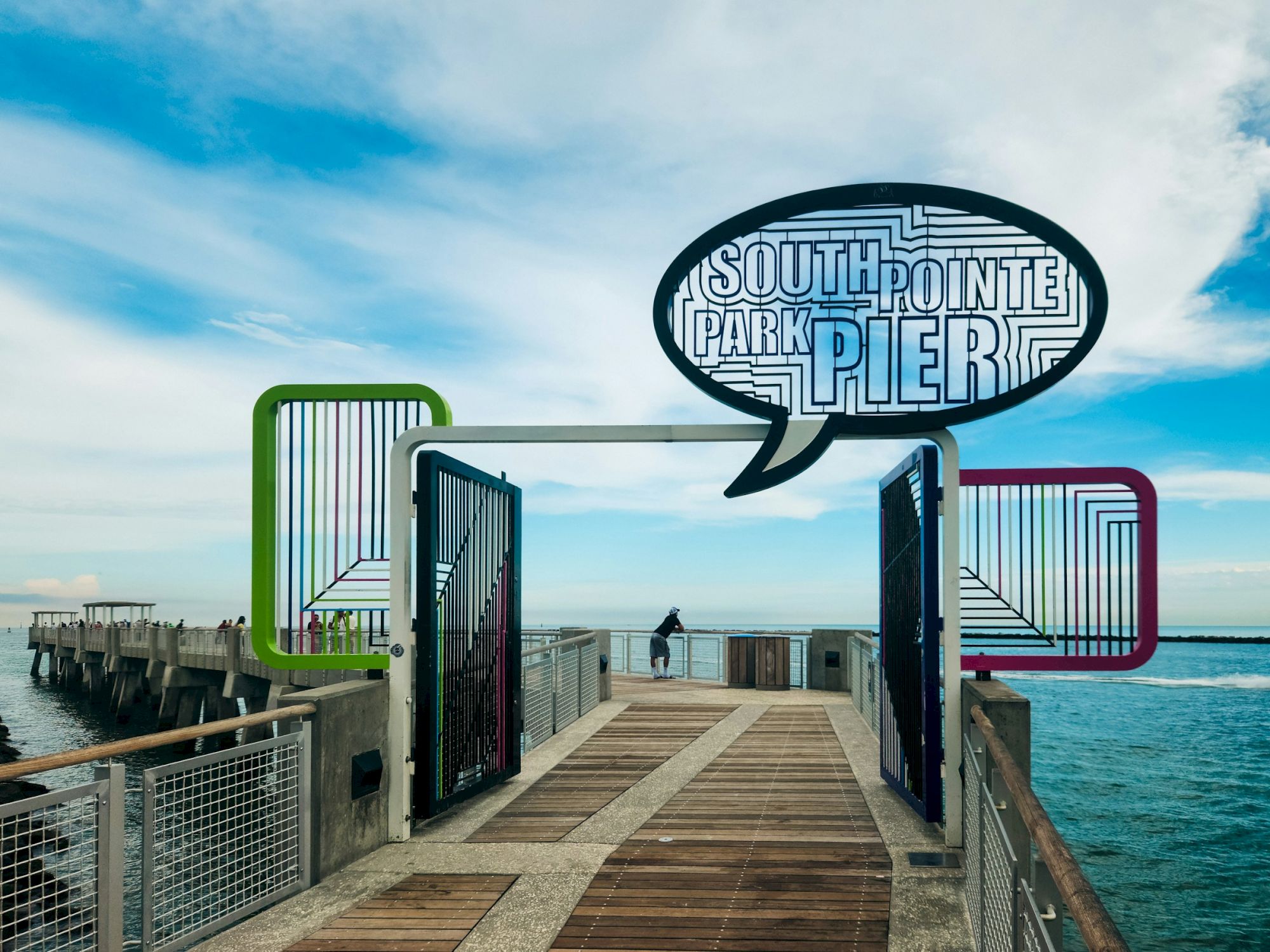 A pier with a colorful sign reading "South Pointe Park Pier" overlooks the ocean under a partly cloudy sky.